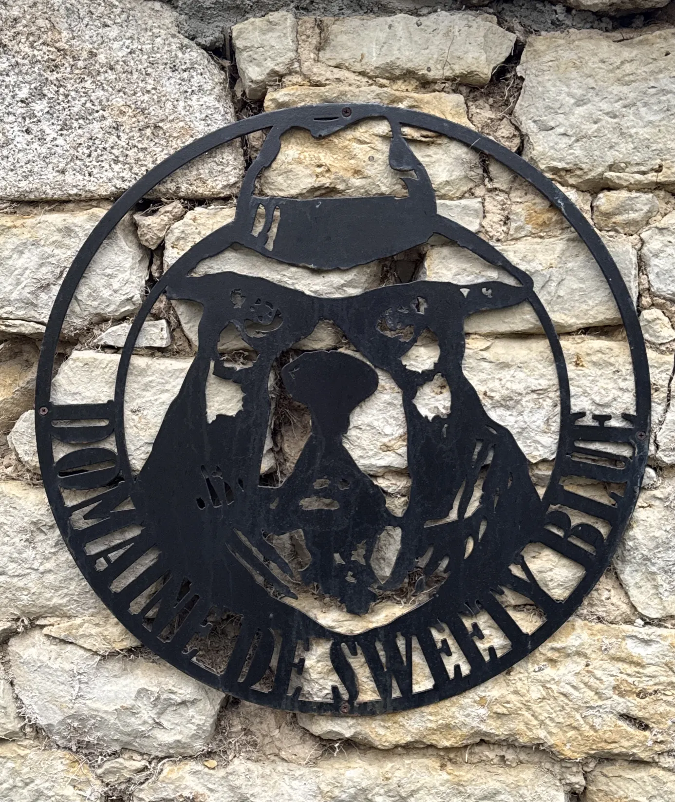Enseigne en métal du Domaine de Sweety Blue représentant une tête d’Am’staff, fixée sur un mur en pierre